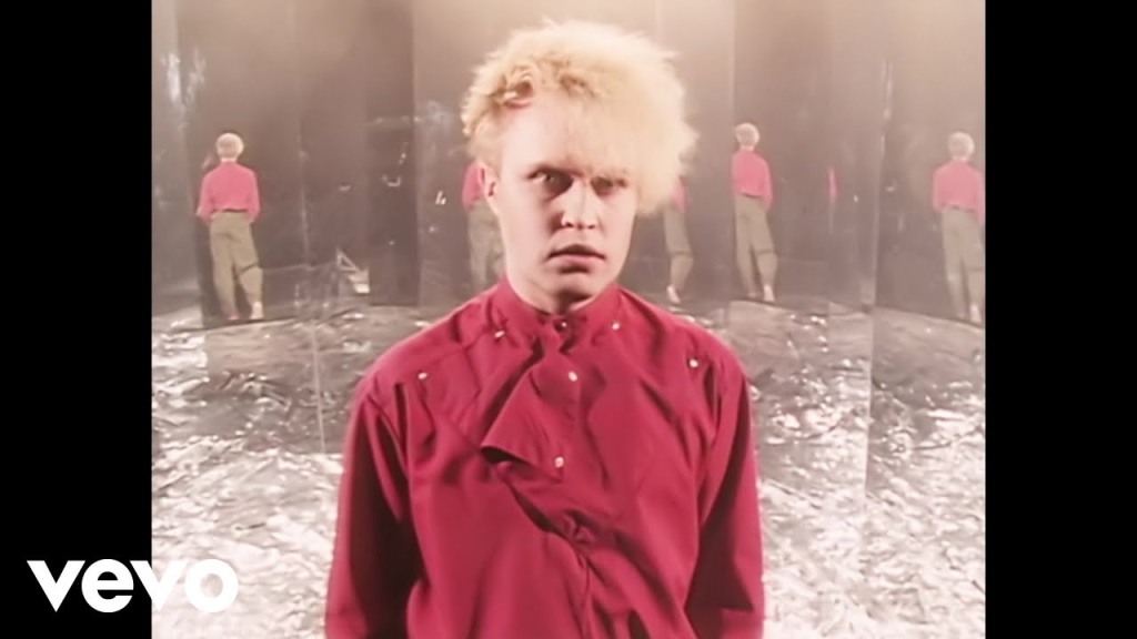 Shot from Flock of Seagull's I Ran music video, featuring the most 80s-looking white guy possible in a bleached bouffant haircut and assymetrical red puffy shirt